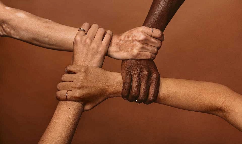 Four hands with varying skin tones grasping the wrist of a different arm.